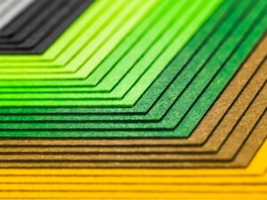 Close-up abstract image of colorful layered paper sheets in green, yellow, and gray creating geometric patterns.