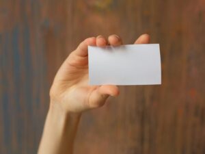 Human hand holding blank white card with wooden background focus on card